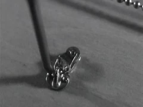 Close-up shows small metal fittings and hooks being attached to a model boat deck.