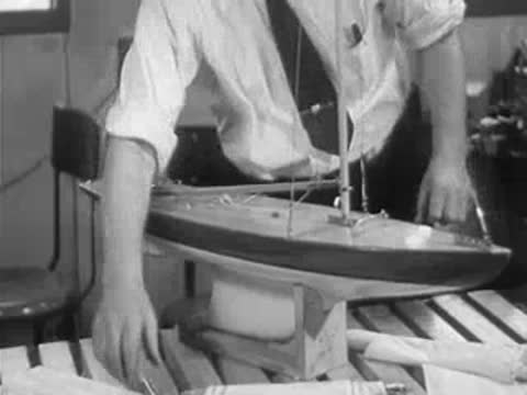 A craftsman puts finishing touches on a large model sailboat in his workshop.