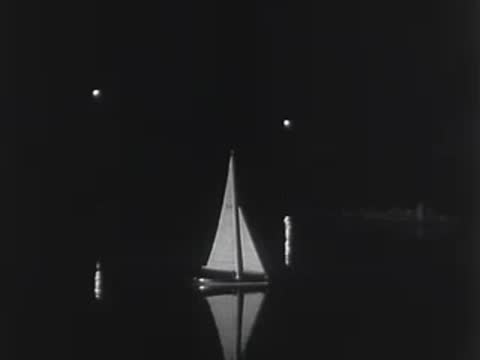 A man approaches a parked car at night near a dark body of water.
