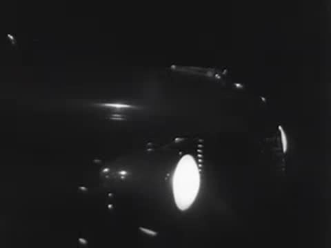 Inside a car at night, a foot presses on the gas pedal as headlights illuminate.