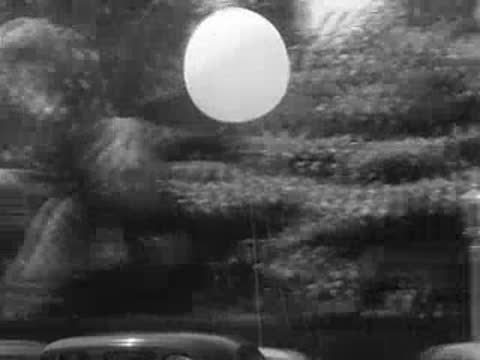 Weather balloon floating past palm trees and traffic on a city street