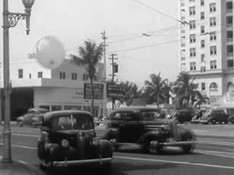 Traffic driving down a city street with palm trees and buildings in the background