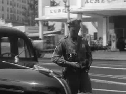 Police officer standing near a vintage car parked at an Acme Lube service station