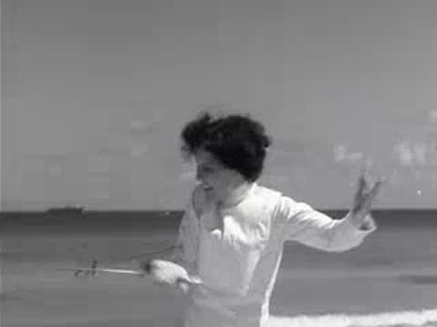 Fencer dueling with another person on beach with ocean in background