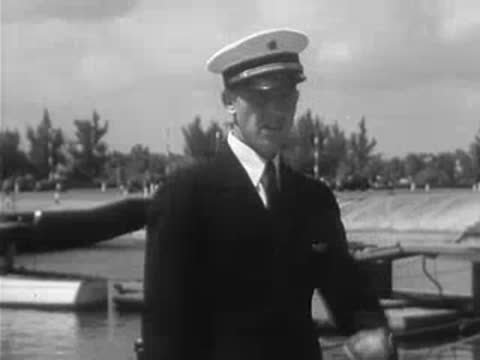 Man in uniform checks his watch, stands by water.