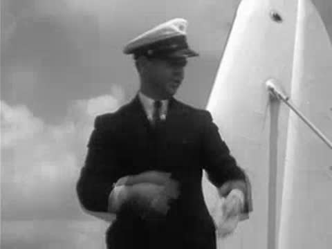 Man in uniform carries boxes, checks clipboard, stands by seaplane.