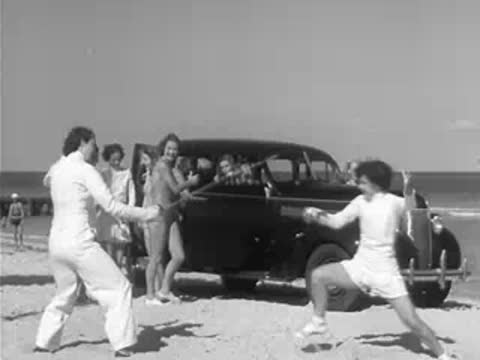 Fencers on beach near parked car with spectators watching