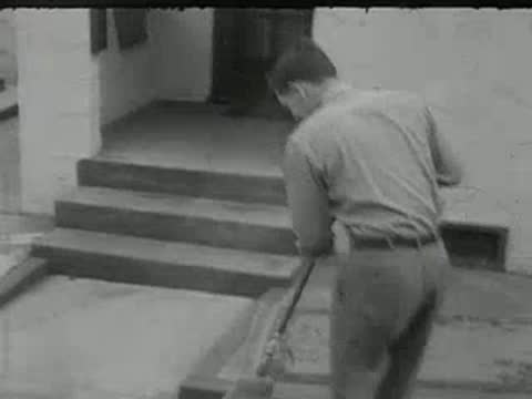 A man sweeping the front steps of a house in vintage work clothes.