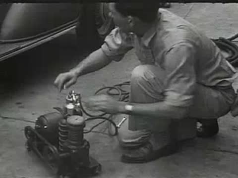 A man kneeling and working on a motor or air compressor outdoors.
