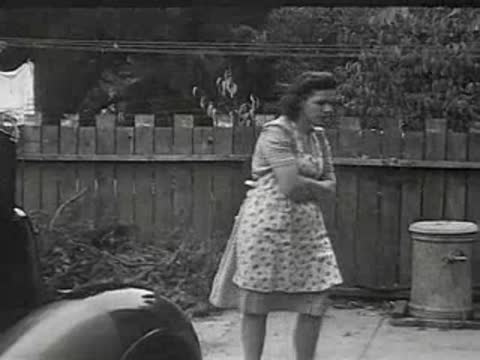 A woman standing by a wooden fence, then walking away.