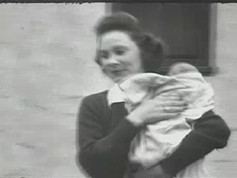 A woman holding a baby wrapped in a blanket outdoors.