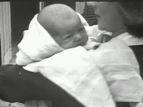 A close-up of a woman holding a sleeping baby wrapped in a blanket.