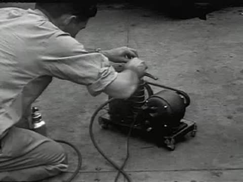 A man kneeling and repairing a motor or air compressor with tools.