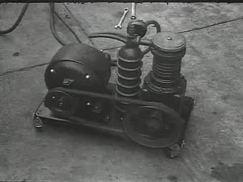 A small black air compressor on wheels with a belt drive system.