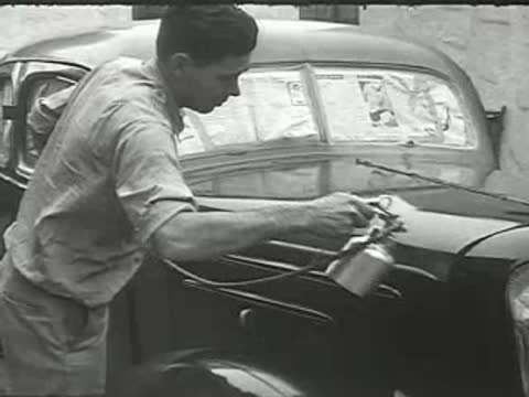 A man spraying paint onto the hood of a vintage car.