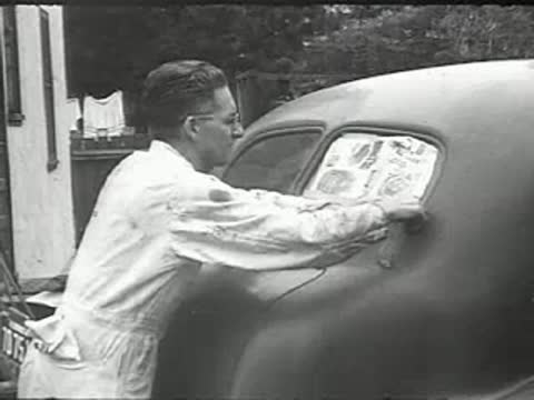 A man removing tape from the rear window of a newly painted car.