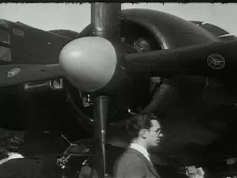 A close-up of a twin-engine airplane propeller with people walking by.