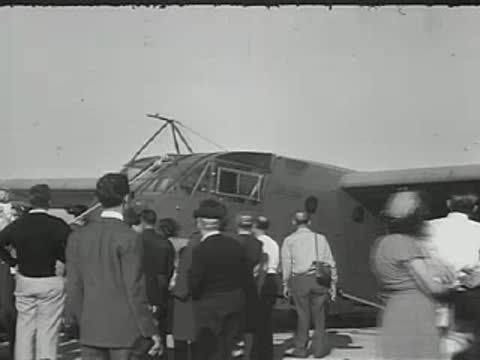 Crowd of people standing near a parked aircraft on a sunny day.