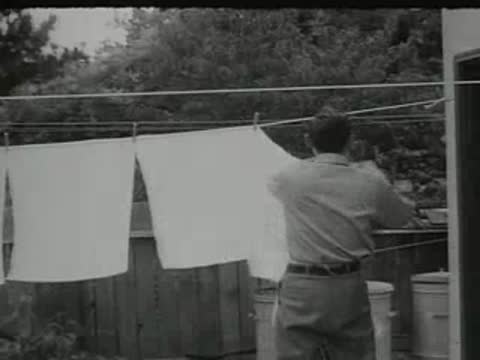 man hanging laundry on a clothesline in a yard