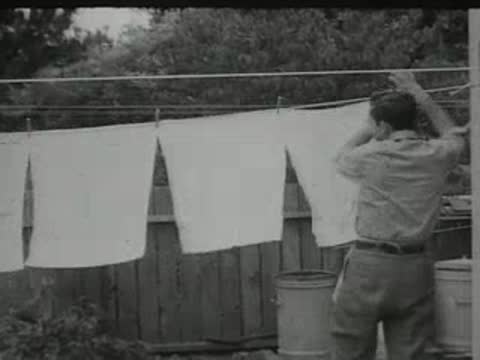 man hanging white laundry on a clothesline outdoors