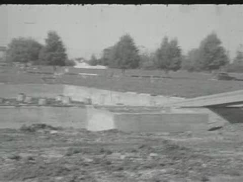 An empty dirt plot with concrete foundation outlines and trees in the background.