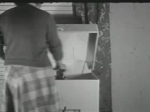 A person in a plaid skirt opens and inspects an appliance indoors.