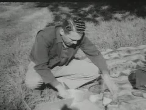 A man kneeling on a picnic blanket unpacks items from a container.