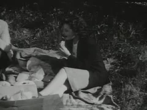 A woman sits on a picnic blanket outdoors eating food.