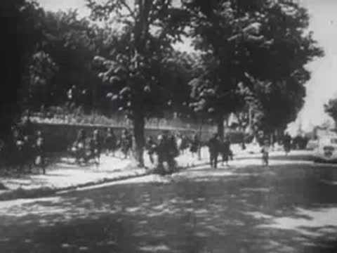 damaged building with smoke and people walking on a tree-lined street
