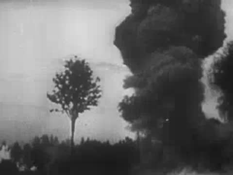smoke rising from explosions behind trees in a rural landscape