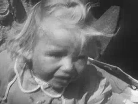 A young blonde child cries while being transported in a cart.