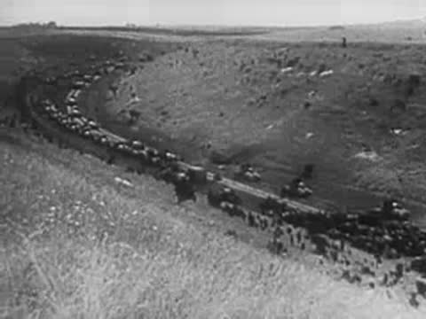 Aerial tracking shot of military convoy winding through a valley road.
