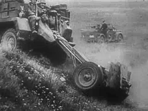 Soldier pushing a stalled car on a slope near military vehicles, World War II