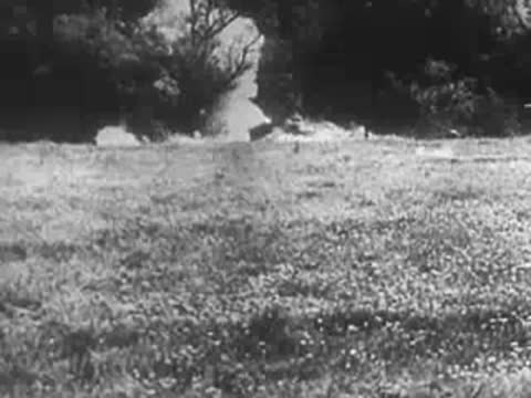 Explosions smoking on a grassy field with treeline in background, World War II