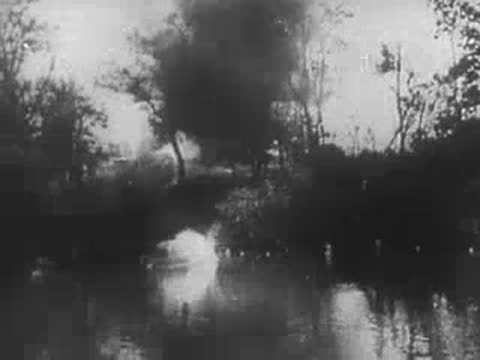 Soldier in helmet watching water body with trees and smoke in background, World War II