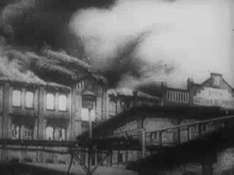 Military aircraft in flight and heavily damaged buildings with smoke.