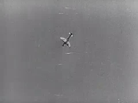 A military aircraft in flight against a bright sky, dropping payload.