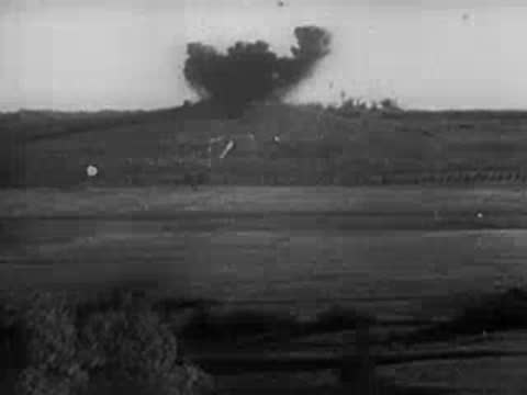 Explosions creating smoke and debris on a distant hill over a landscape.
