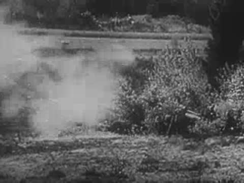 German soldiers operating a field artillery piece amidst bushes and smoke.