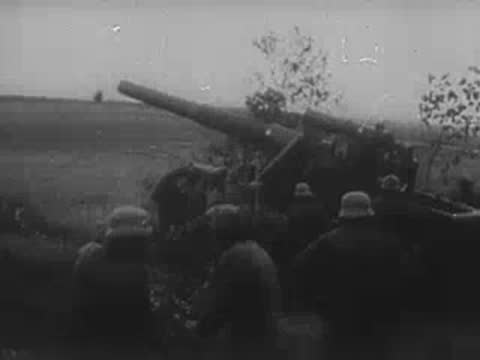 German soldiers taking cover by trees and operating a heavy artillery gun.