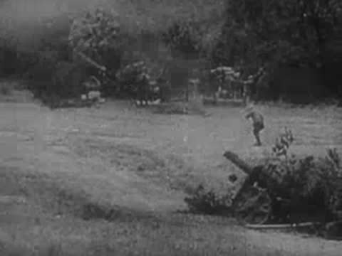 Soldiers loading and operating a large artillery piece in a grassy field.