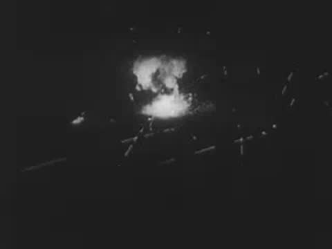 Explosions flashing brightly across a dark landscape at night or dusk.