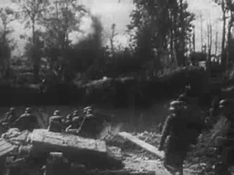 German soldiers advancing along a riverbank and taking cover near trees.