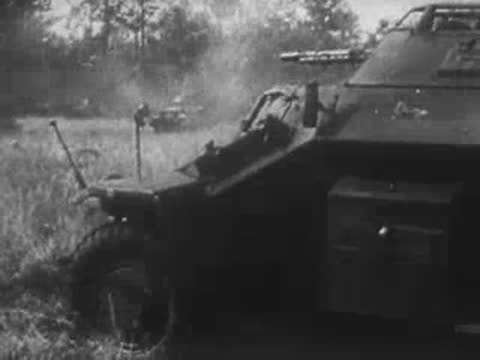 An armored car near a river where soldiers in small boats cross.