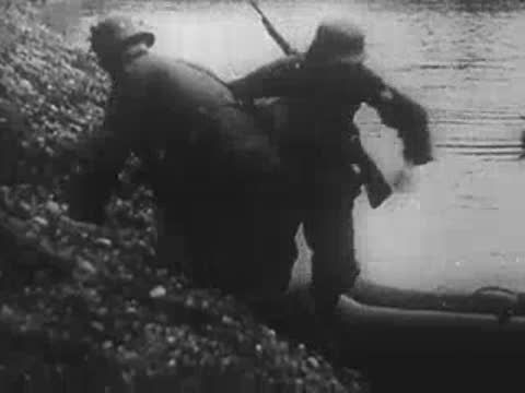 German soldiers sliding down a muddy riverbank to board small boats.