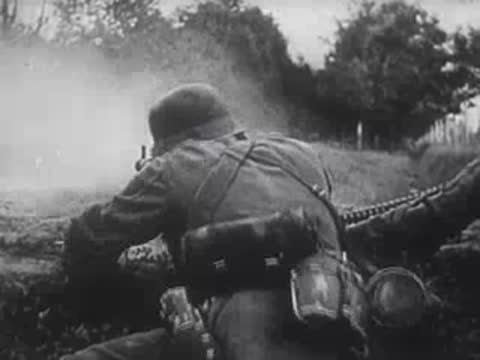 German machine gunner firing from a prone position in a field.