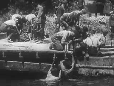 Construction workers building a pontoon bridge over a river.