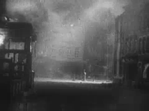 City street at night with damaged, burning buildings and smoke.