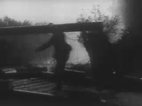 Soldiers carrying materials near a pontoon bridge in smoke.