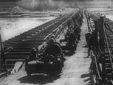 Military vehicles and troops crossing a pontoon bridge over water.